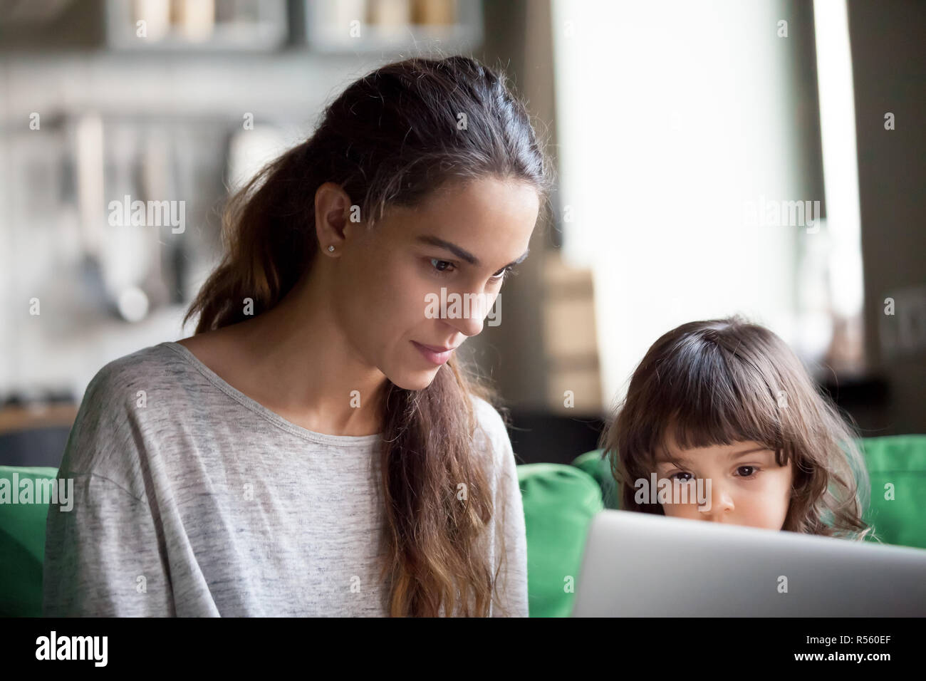 Ernsthafte alleinerziehende Mutter mit Laptop zusammen mit Tochter Stockfoto