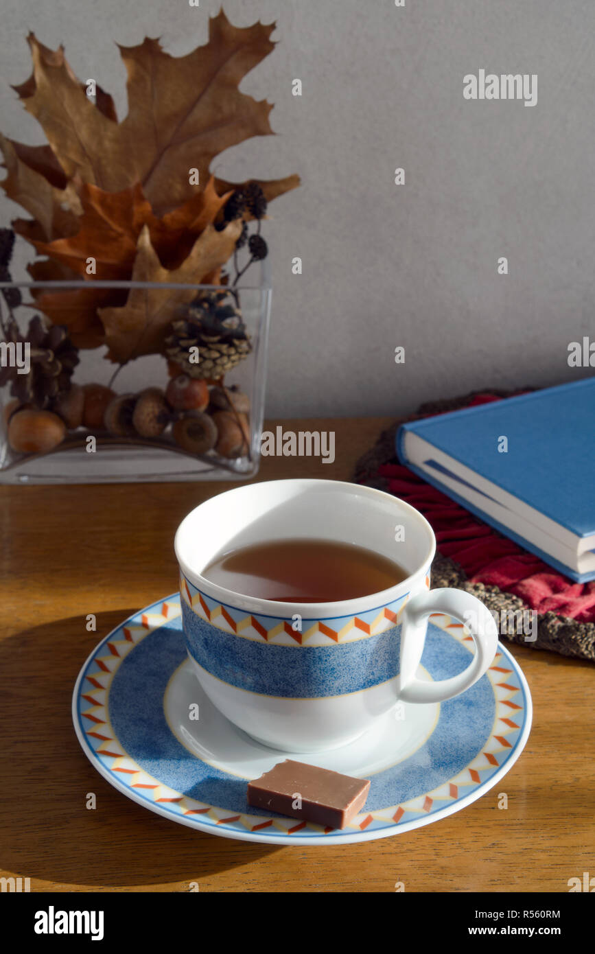 Noch immer leben bei einer Tasse Tee und einem Stück Schokolade, im Hintergrund ein Buch und Dekoration im Herbst Laub (Tasse mit Untertasse getrennt) Stockfoto