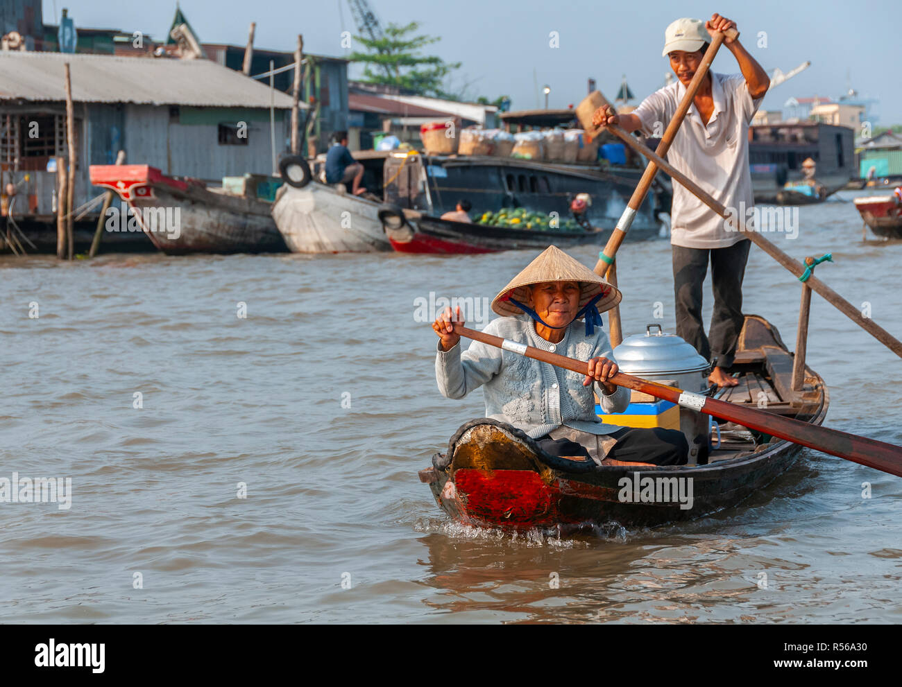 Ältere Frauen und Jüngere männliche Paddeln durch die Cai Rang Floating Market, Can Tho, Vietnam, Verkauf von Speisen an die Händler aus Ihren hölzernen Boot Stockfoto