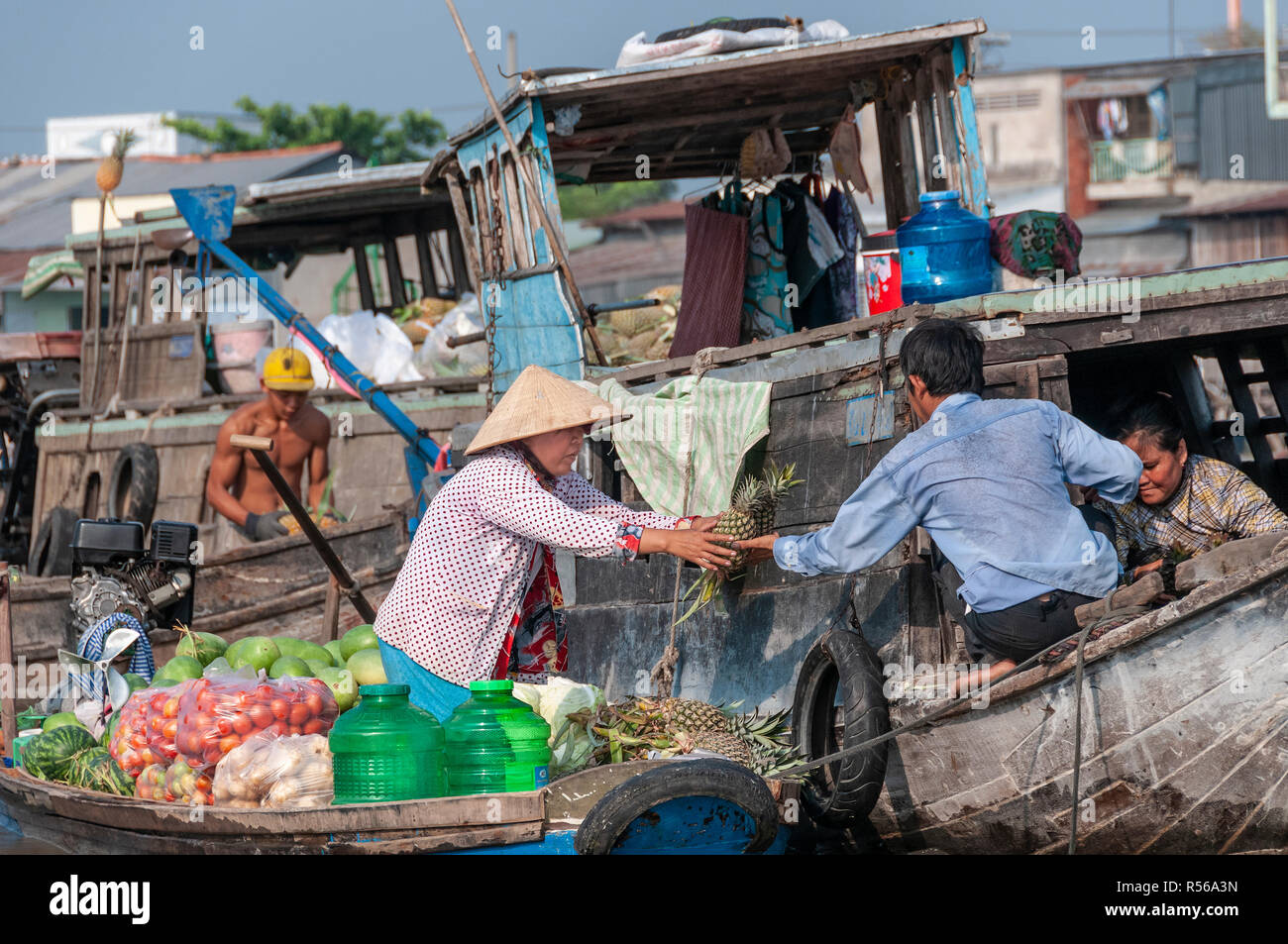Weibliche boatwoman Verkauf Hände produzieren über eine Ananas an einen Käufer auf einem anderen Holz- Boot an der Cai Rang Floating Market, Can Tho Provinz, Vietnam Stockfoto