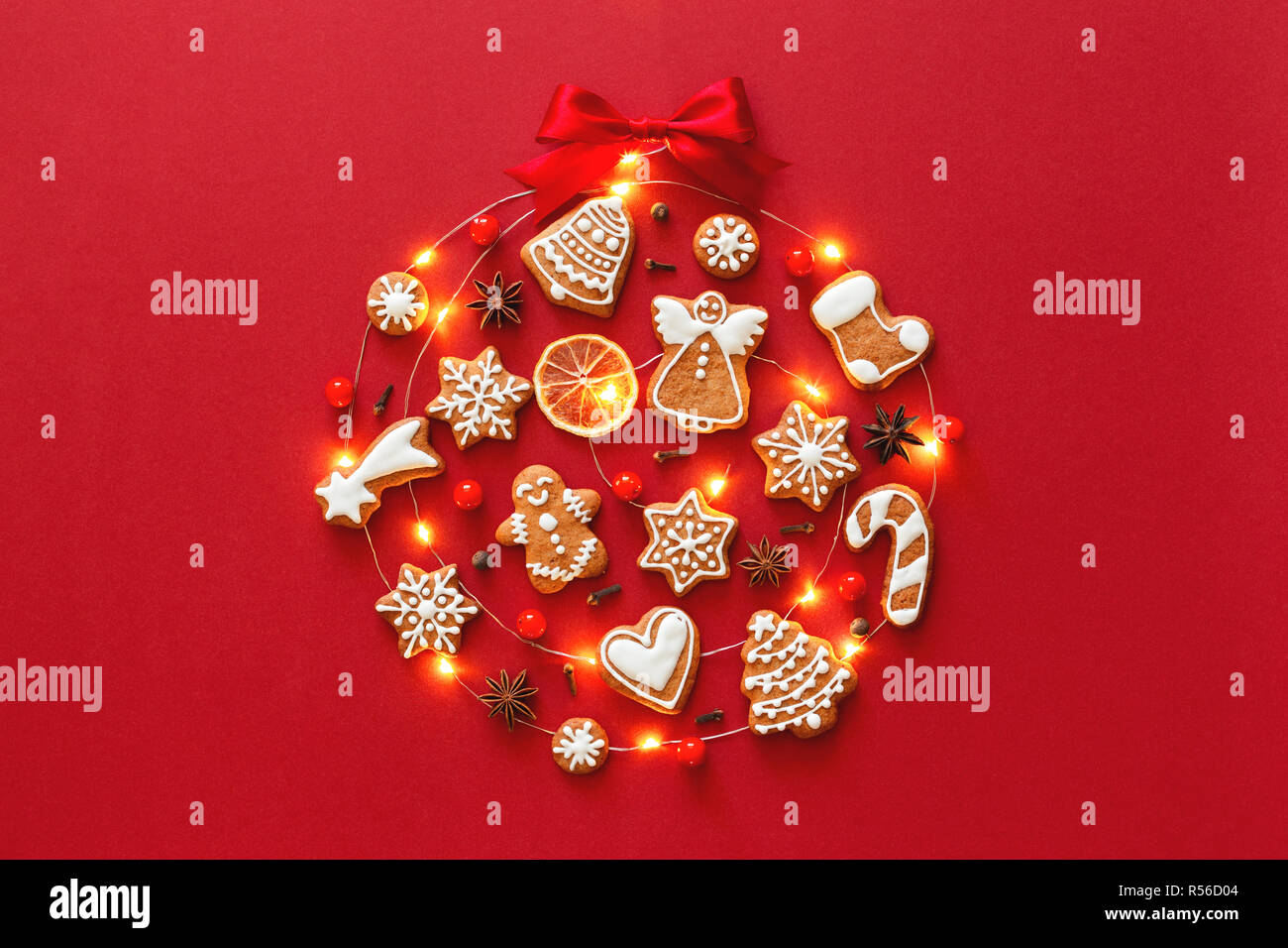 Creative Christmas Ball aus iced Lebkuchen cookies, Anis Sterne, Beeren, orange Chips, dekoriert mit roten Schleife auf rotem Hintergrund. Neues Jahr Grußkarten-Konzept. Ansicht von oben. Stockfoto