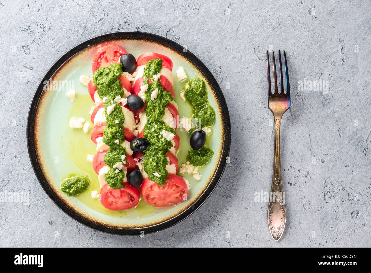 Tomaten und Mozzarella Caprese Salat und Pesto Sauce mit Oliven auf grau Tisch serviert mit Gabel. Essen italienische Vorspeise Stockfoto