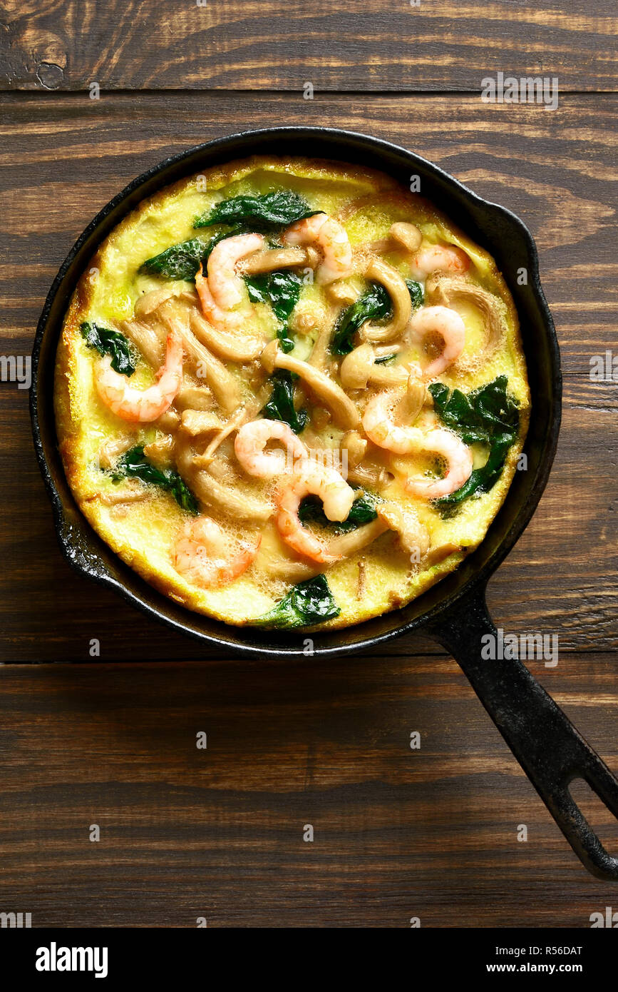 Schmackhafte Pilze, Spinat, Garnelen frittata (gebratene Eier mit Gemüse) in der Pfanne auf Holz- Hintergrund. Ansicht von oben, flach Stockfoto