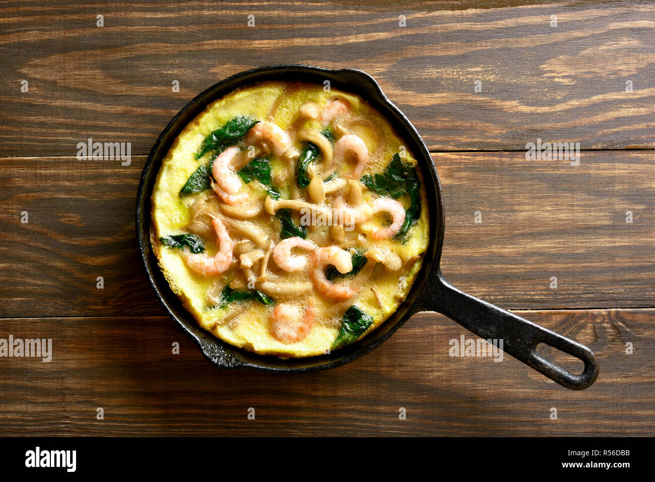 Omelette, Pilzen und Spinat frittata mit Garnelen in einer Pfanne auf Holz- Hintergrund. Ansicht von oben, flach Stockfoto