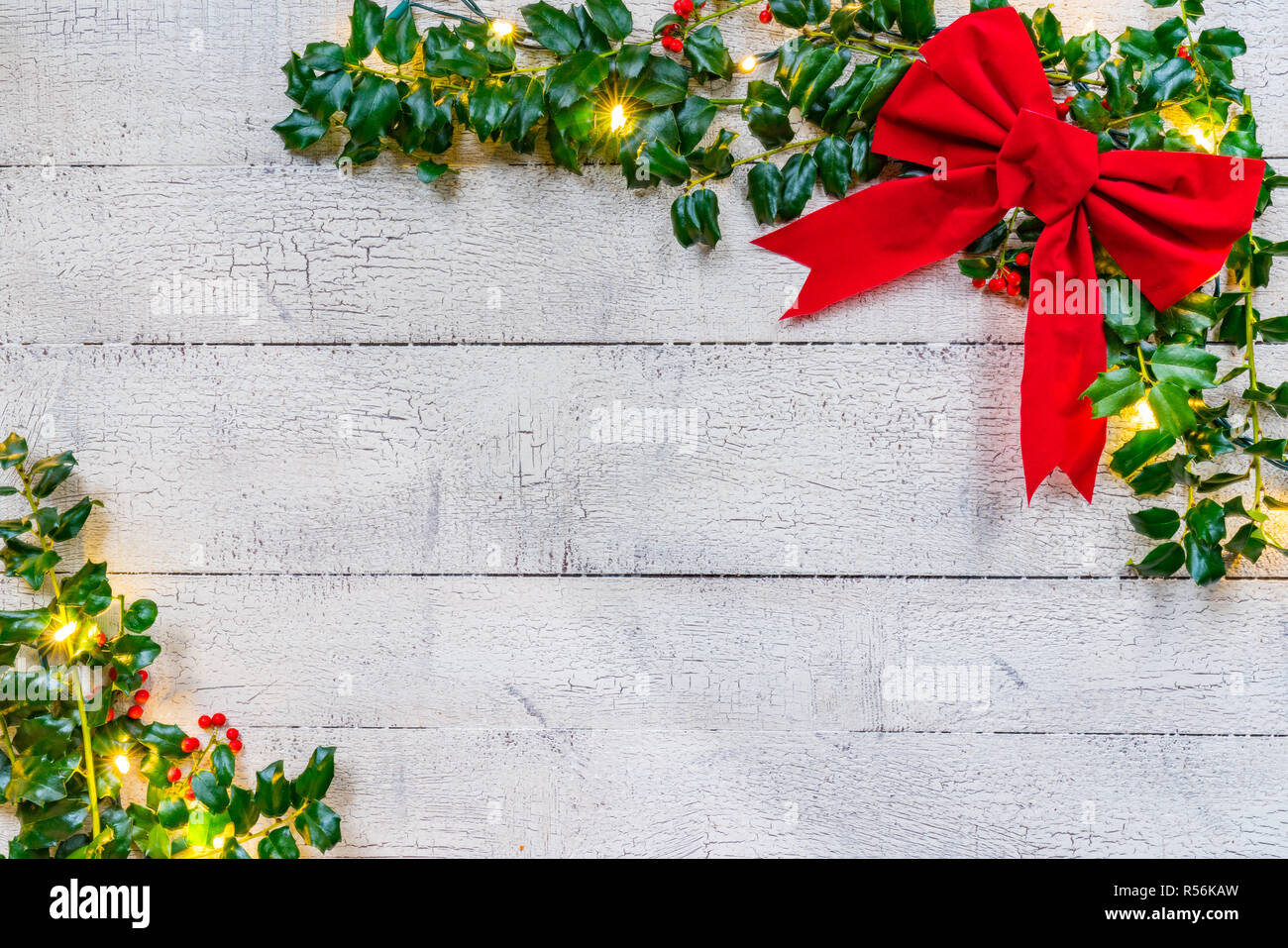 Weihnachten Holly mit Bogen, die Scheinwerfer und die Beeren auf einem weißen Holz Hintergrund Stockfoto