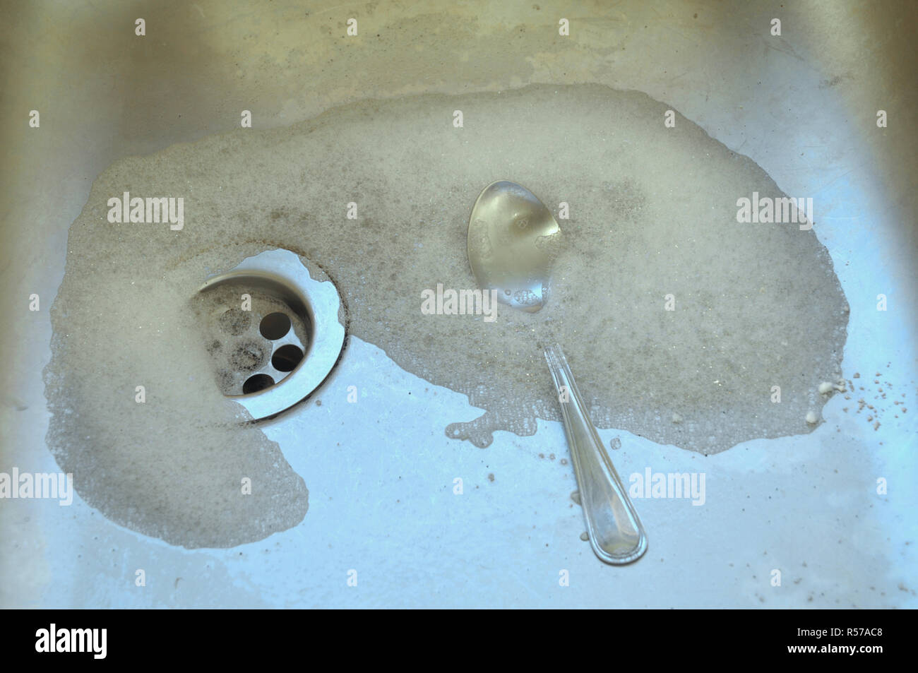 Eine silberne Teelöffel in ein Spülbecken halb liegend begraben in Spülmittel seifenlösungen. Stockfoto