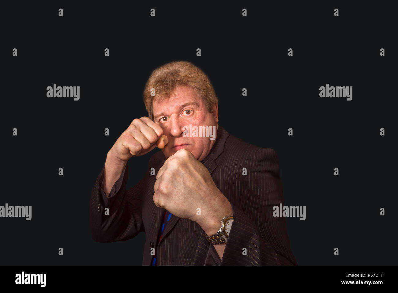 Studio shot der verärgerten älterer Geschäftsmann mit Faust heben gegen den dunklen Hintergrund Stockfoto