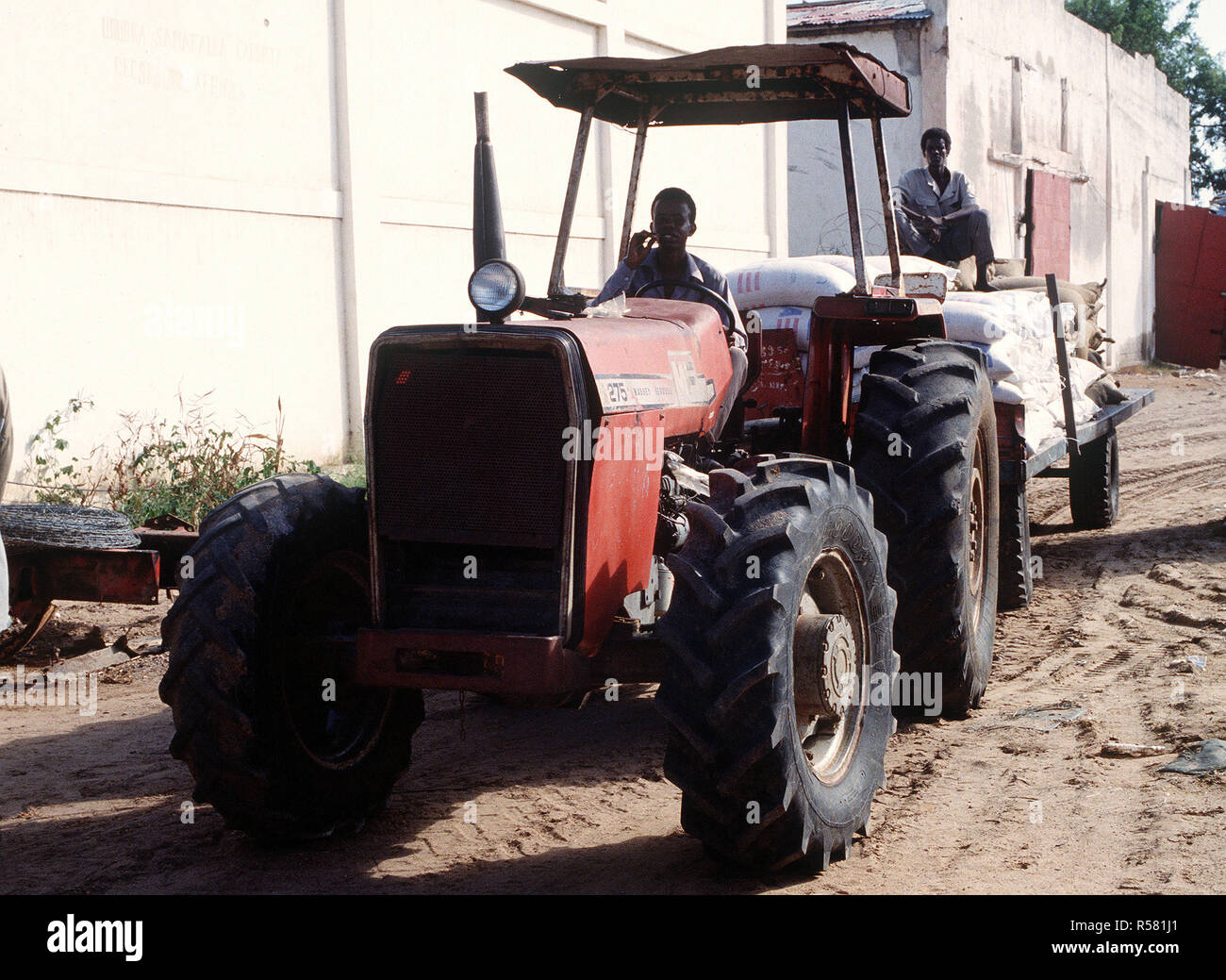 1993 - Ein somalischer Mann fährt ein Traktor zieht einen Anhänger voll von Lieferungen an das Essen Lager in Kismayo. Nach dem Essen ist entfallen, es in der ganzen Stadt durch die Vereinten Nationen zu essen Distributionszentren in Somalia geliefert wird zur Unterstützung der Operation weiterhin Hoffnung. Stockfoto