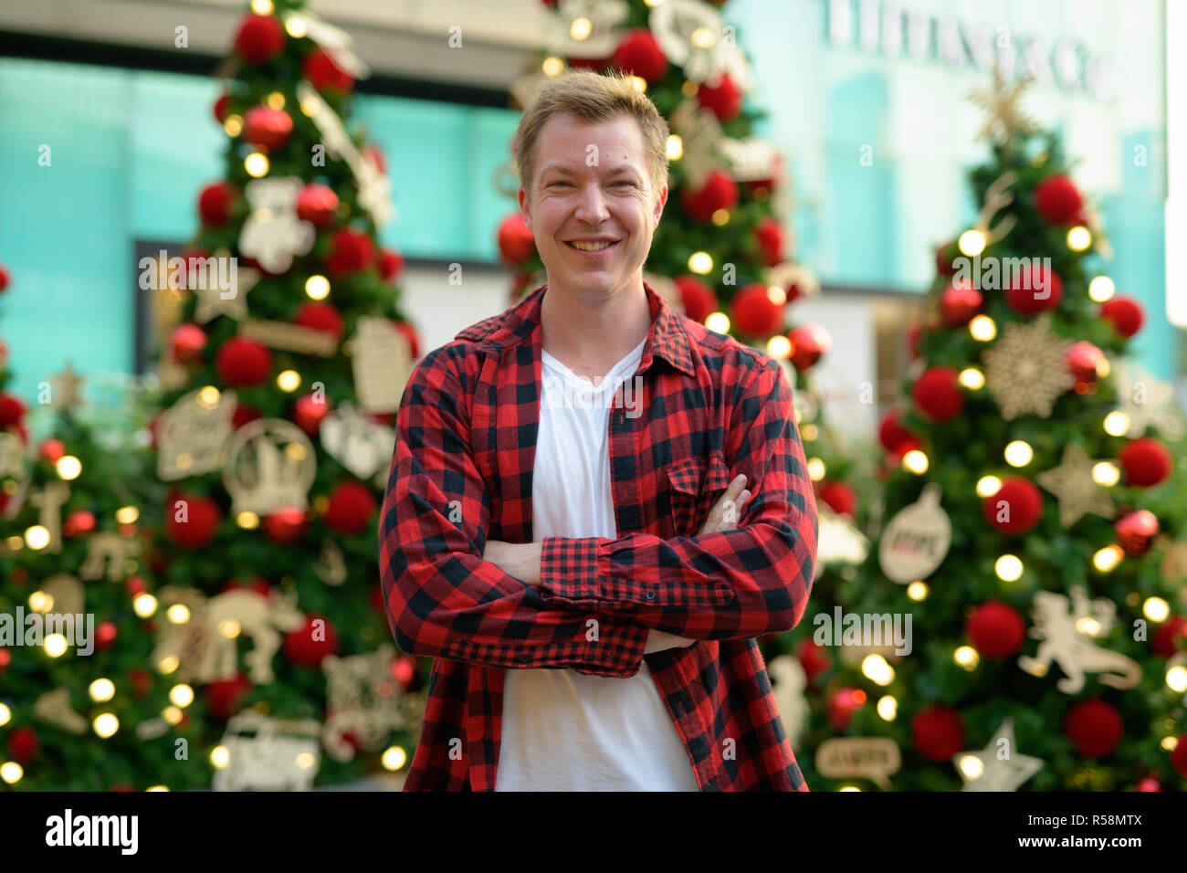 Junge Happy Hippie Mann lächelnd gegen Beleuchtete Weihnachtsbäume im Freien Stockfoto
