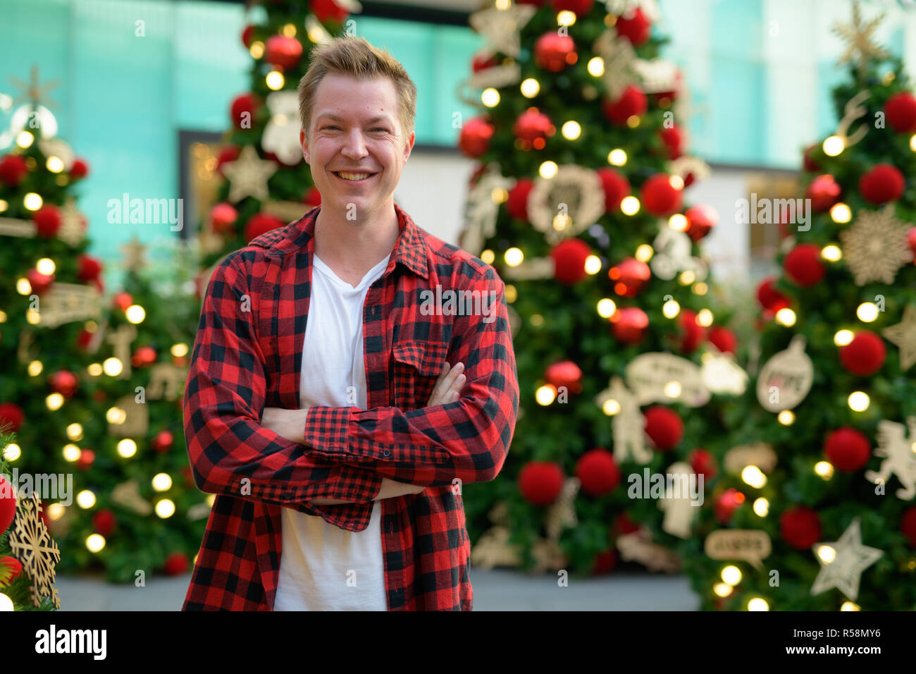 Junge schöne Hipster Mann lächelnd gegen Beleuchtete Weihnachtsbäume im Freien Stockfoto