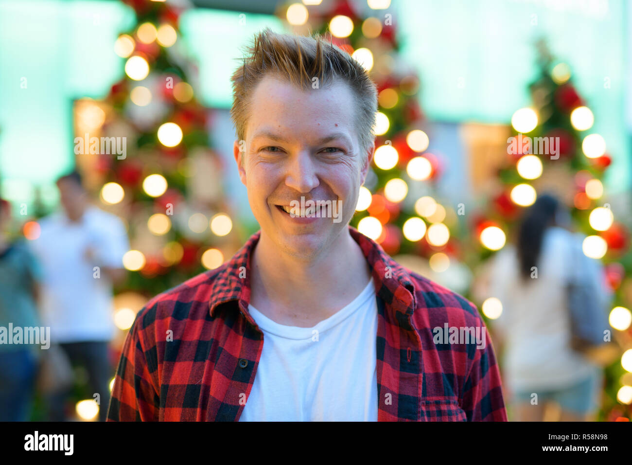 Gesicht der jungen Happy Hippie Mann lächelnd gegen Weihnachtsbäume im Freien Stockfoto
