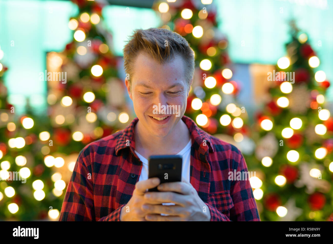 Junge Happy Hippie Mann mit Phone gegen Weihnachtsbäume im Freien Stockfoto