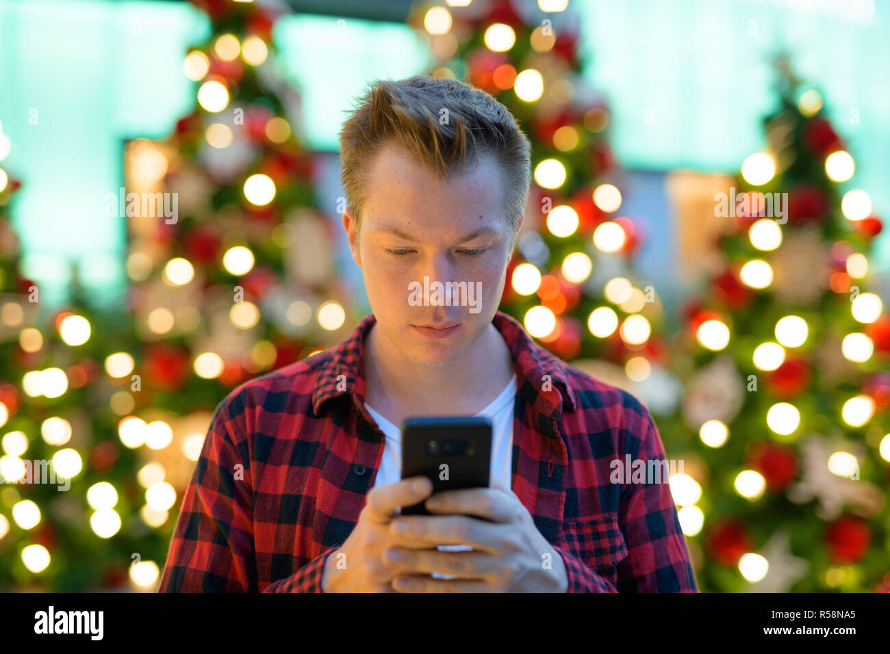 Jungen gutaussehenden Mann Hipster mit Phone gegen Weihnachtsbäume im Freien Stockfoto