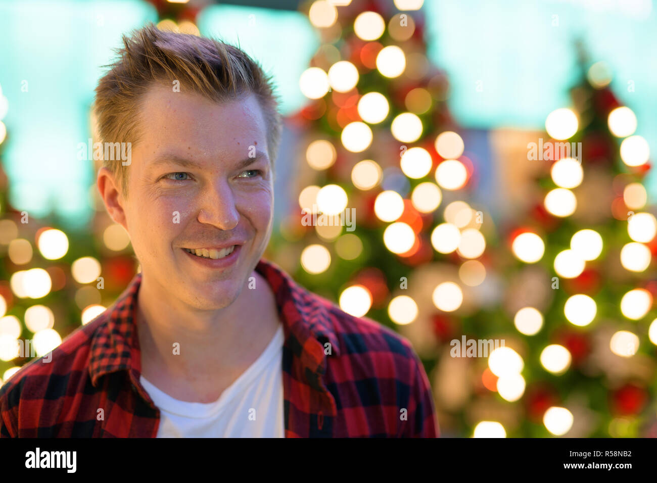 Junge glücklich lächelnd und Denken gegen Weihnachtsbäume im Freien Stockfoto