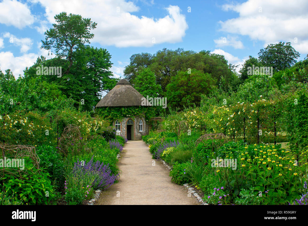 Das 19. Jahrhundert strohgedeckten runden Haus, umgeben von schönen Blumenbeeten und Schotterwege, das in der ummauerten Garten in West Dean Gärten in West Sussex Stockfoto
