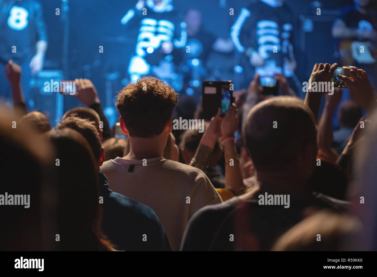 Konzert der Menge mit erhobenen Armen, Silhouetten von Menschen mit Smartphones. Musiker auf einer beleuchteten Bühne. Stockfoto