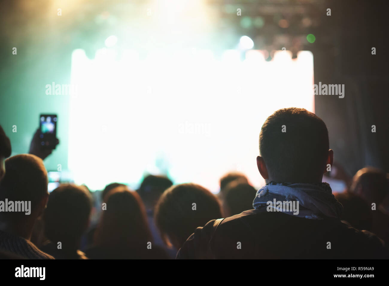 Konzert der Menge mit erhobenen Armen, Silhouetten von Menschen mit Smartphones. Musiker auf einer beleuchteten Bühne. Stockfoto