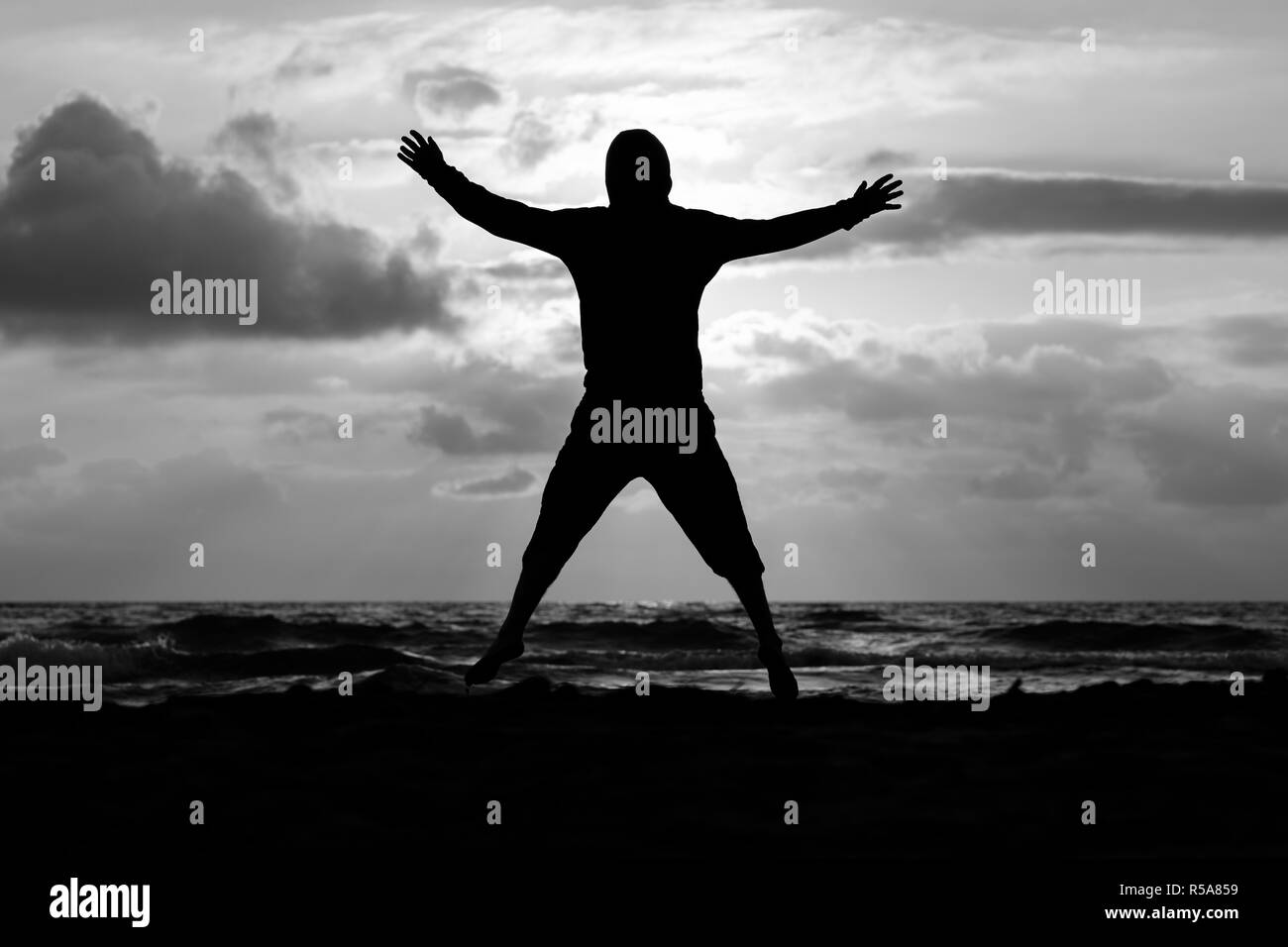 Mann springt bei Sonnenuntergang am Meer, Schwarz und Weiß Stockfoto