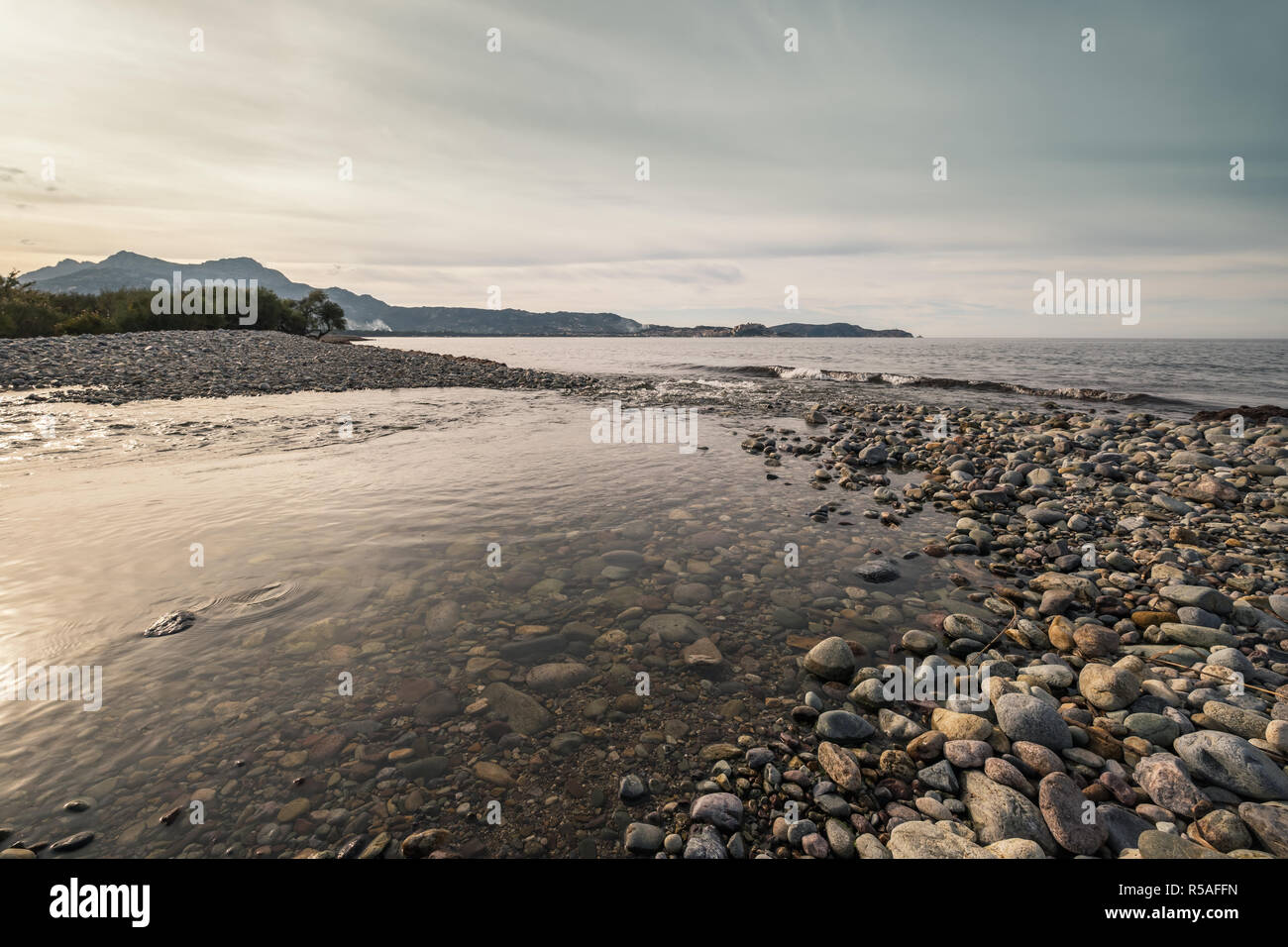 Eine seichte Fluss verbindet das Mittelmeer auf einem Kieselstrand in Korsika mit der Zitadelle von Calvi in der Ferne Stockfoto