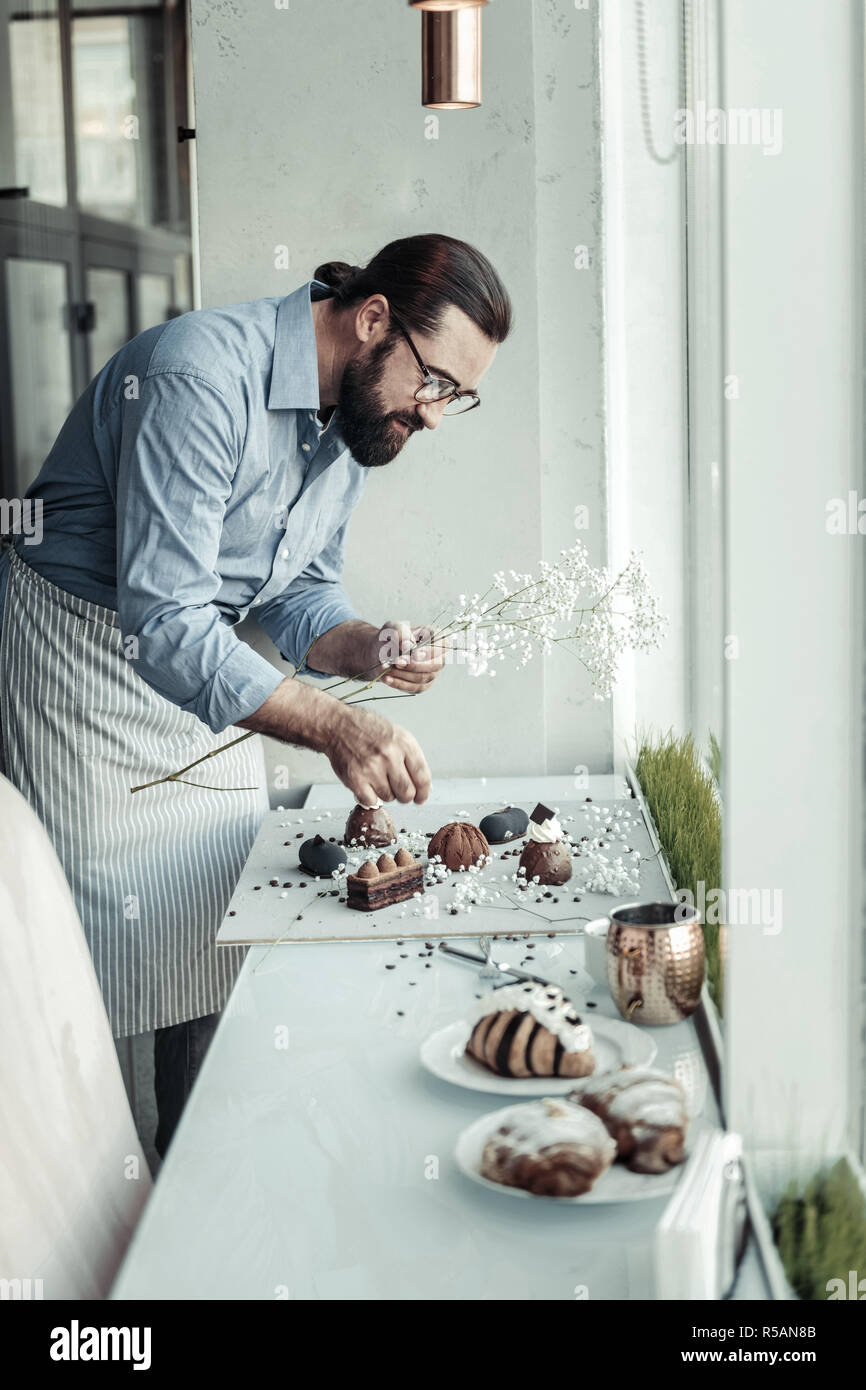 Essen Ästhetik. Ernsthafte intelligenter Mann beugte sich über die Platte mit Kuchen, während Sie verzieren Stockfoto