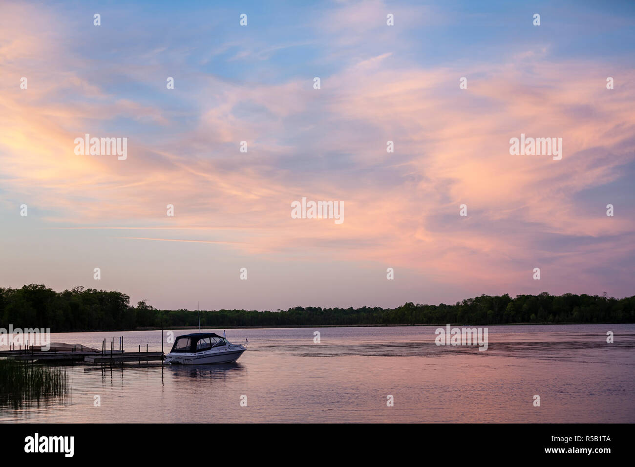 Ruhigen See bei Sonnenaufgang, mit einem kleinen Motorboot bis zu einem Dock gebunden. Stockfoto