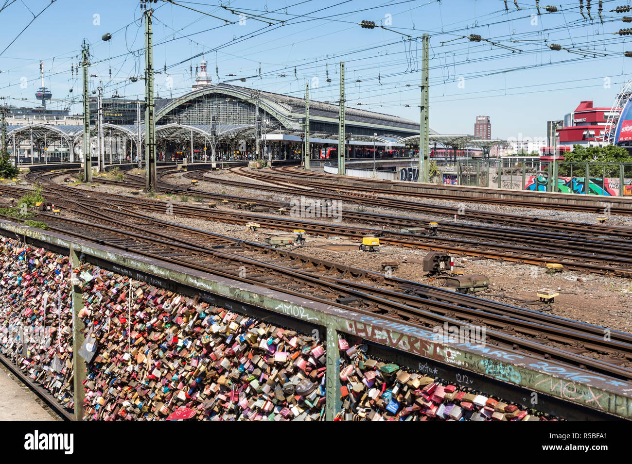 Köln, Deutschland. Liebe Schlösser am Geländer der Hohenzollern Brücke über den Rhein. Bahnhof im Hintergrund. Stockfoto