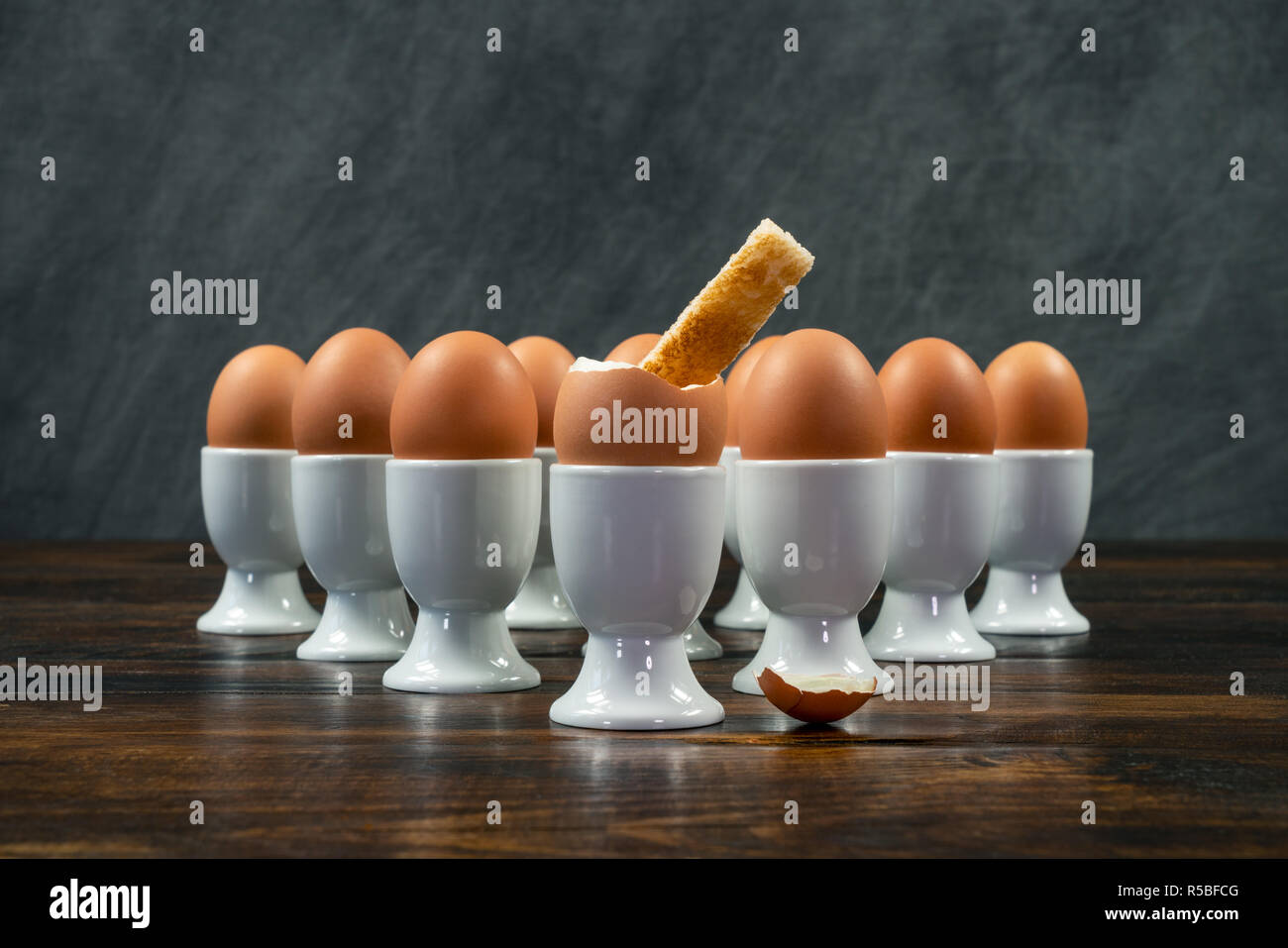 Toast Soldat eingetaucht in ein gekochtes Ei einer Gruppe von Eiern in Weiß Eierbecher auf einem Holztisch Stockfoto