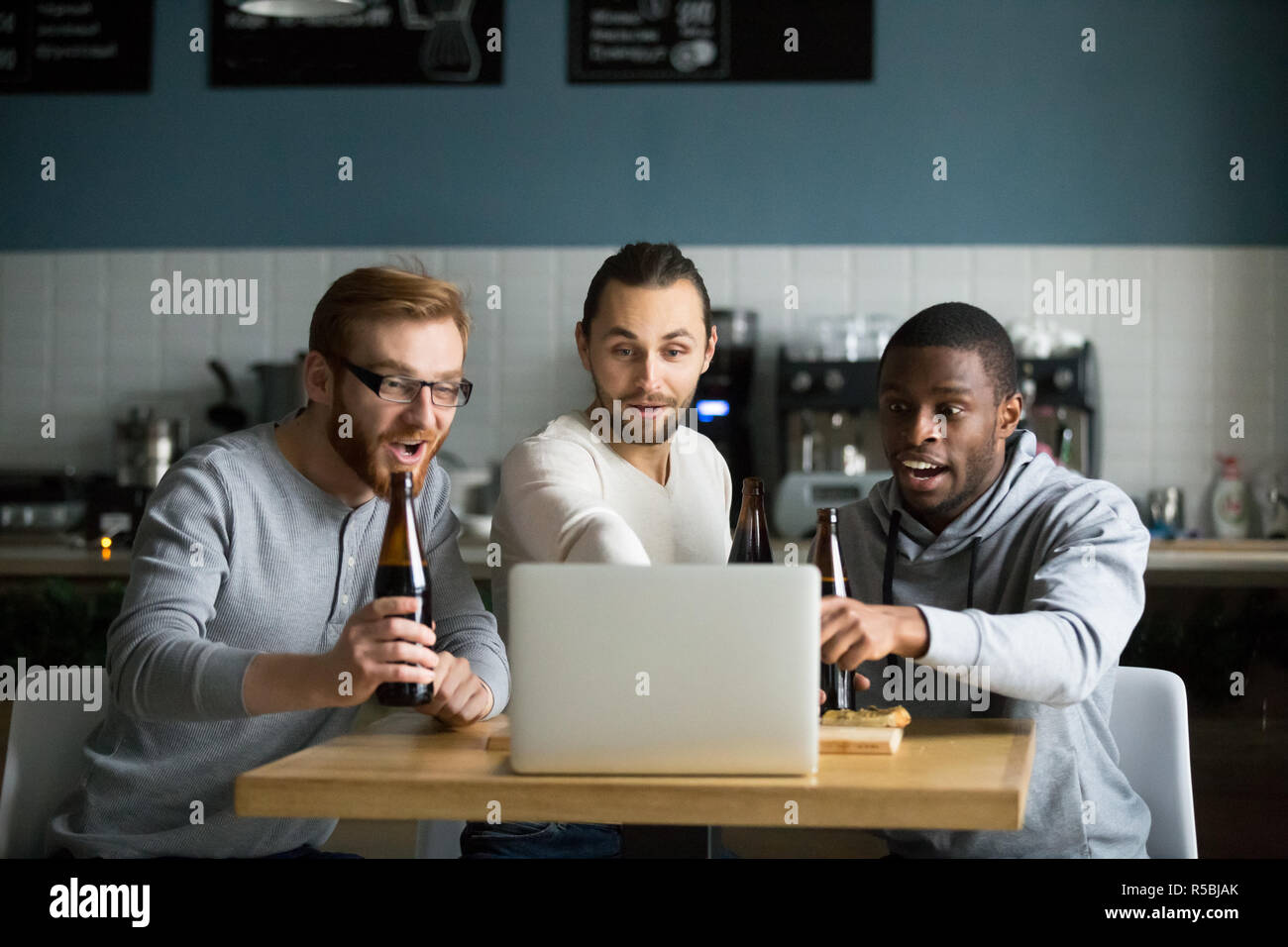 Diverse Freunde hängen in Cafe trinken Bier, online Spiel am Laptop, multiethnischen Männer jubeln Fußball Team genießen Spiel im Pub sitzen Stockfoto
