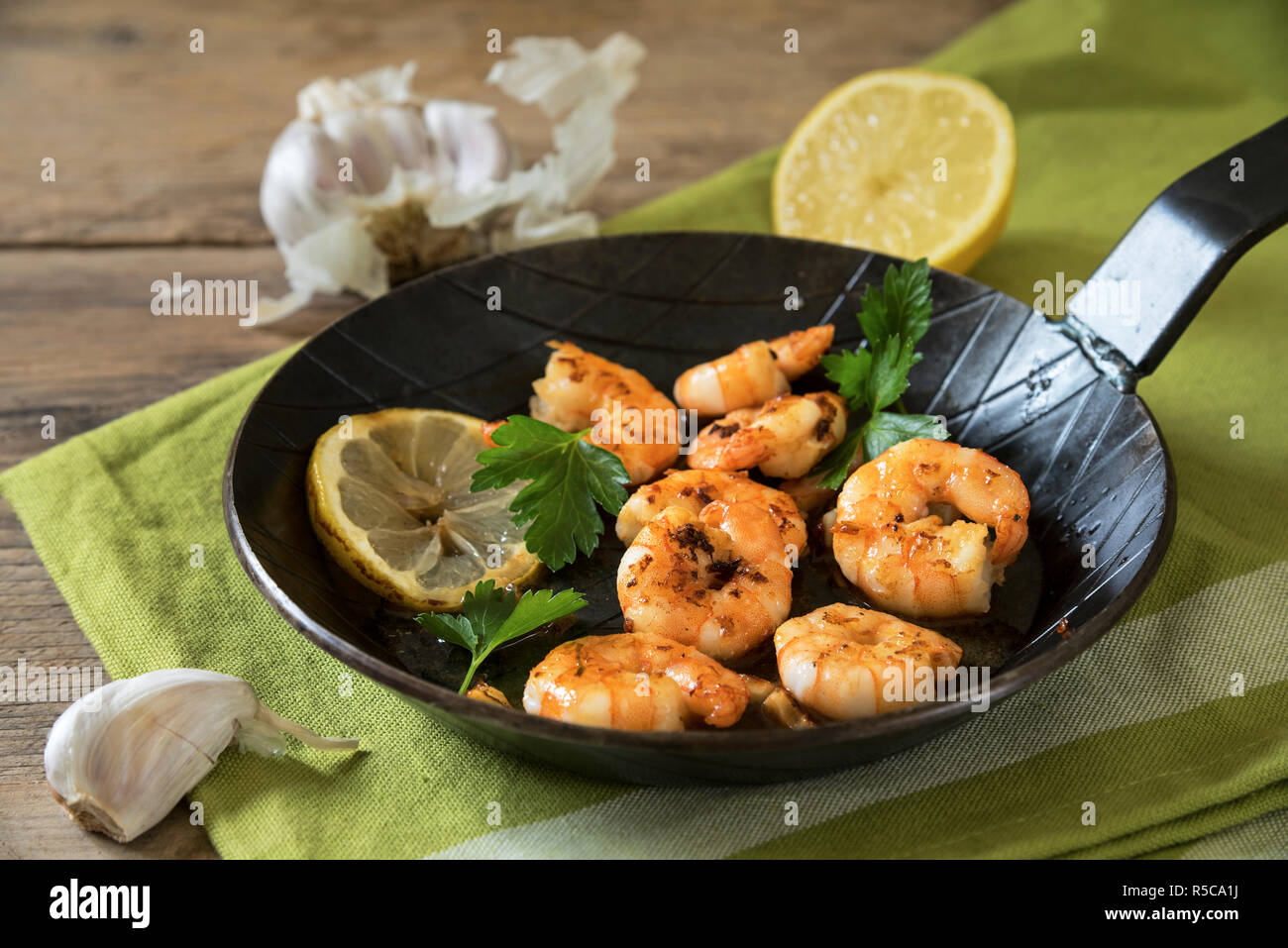 Gebratene King Tiger Garnelen mit Knoblauch, Zitrone und italienische Petersilie in einem schwarzen eiserne Pfanne auf einem grünen Serviette und rustikalem Holz, ausgewählte konzentrieren Stockfoto