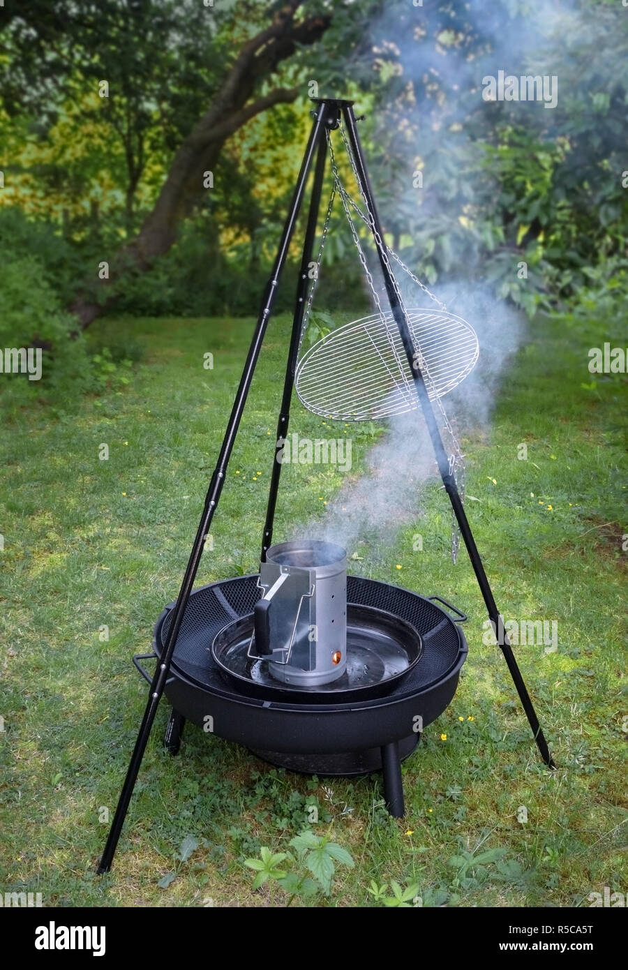 Rauchender Grill Holzkohle Chimney Starter auf einem schwarzen Stativ schwenken Grill im Garten Stockfoto