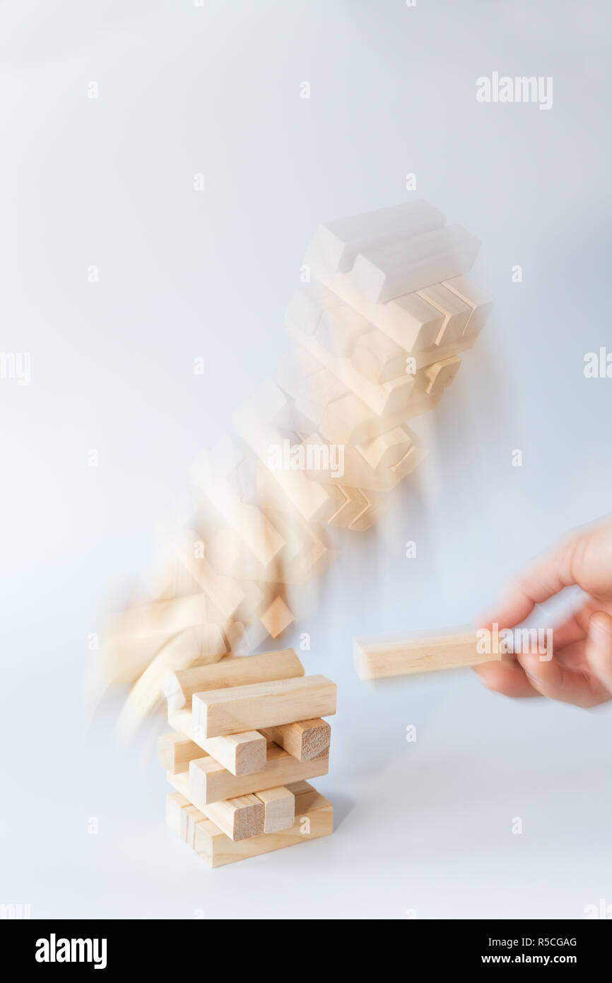 Des Menschen Hand einen Block von einer instabilen Turm von Holzblöcken, wodurch es zu fallen. Konzept Foto von Risiken und Scheitern. Hellgrauen Hintergrund Stockfoto