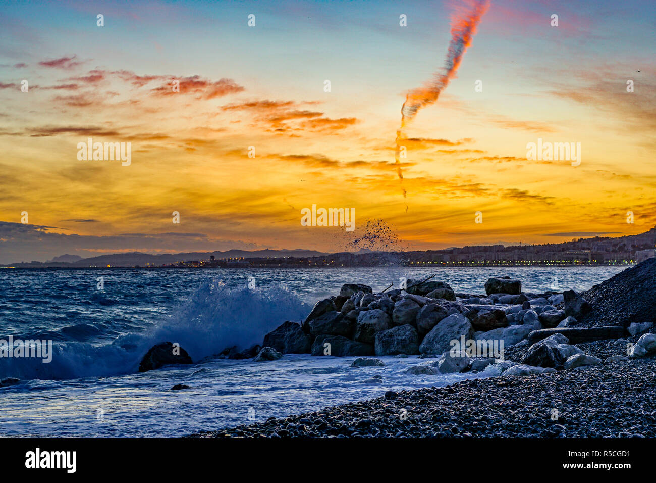 Sonnenuntergang über der Baie des Anges und die Promenade des Anglais: Wellen und Felsen am Strand in Nizza Provence Cote D'Azur Frankreich Stockfoto