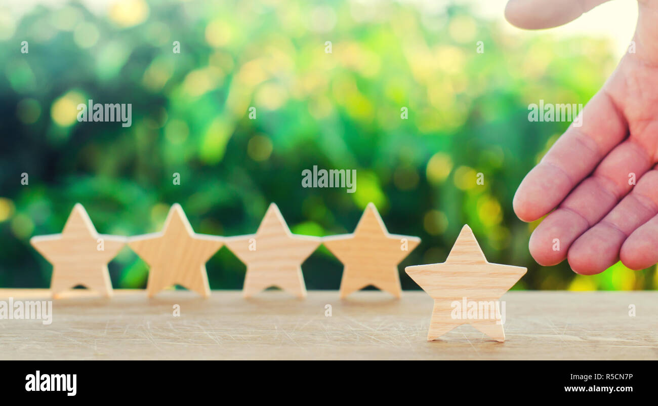 Hand weist auf die fünfte Holz- Stern. Der fünfte Stern erhalten. Das Konzept der Bewertung von Hotels und Restaurants, die Bewertung der Kritiker und Besucher. Stockfoto