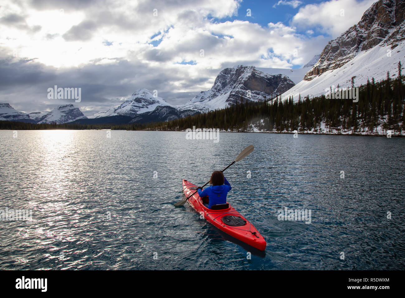 Abenteuerliche Mädchen Kajak in einem Gletscher See durch die Kanadischen Rockies während eines bewölkten Morgen umgeben. An Bow Lake, Banff, Alberta, Kanada. Stockfoto