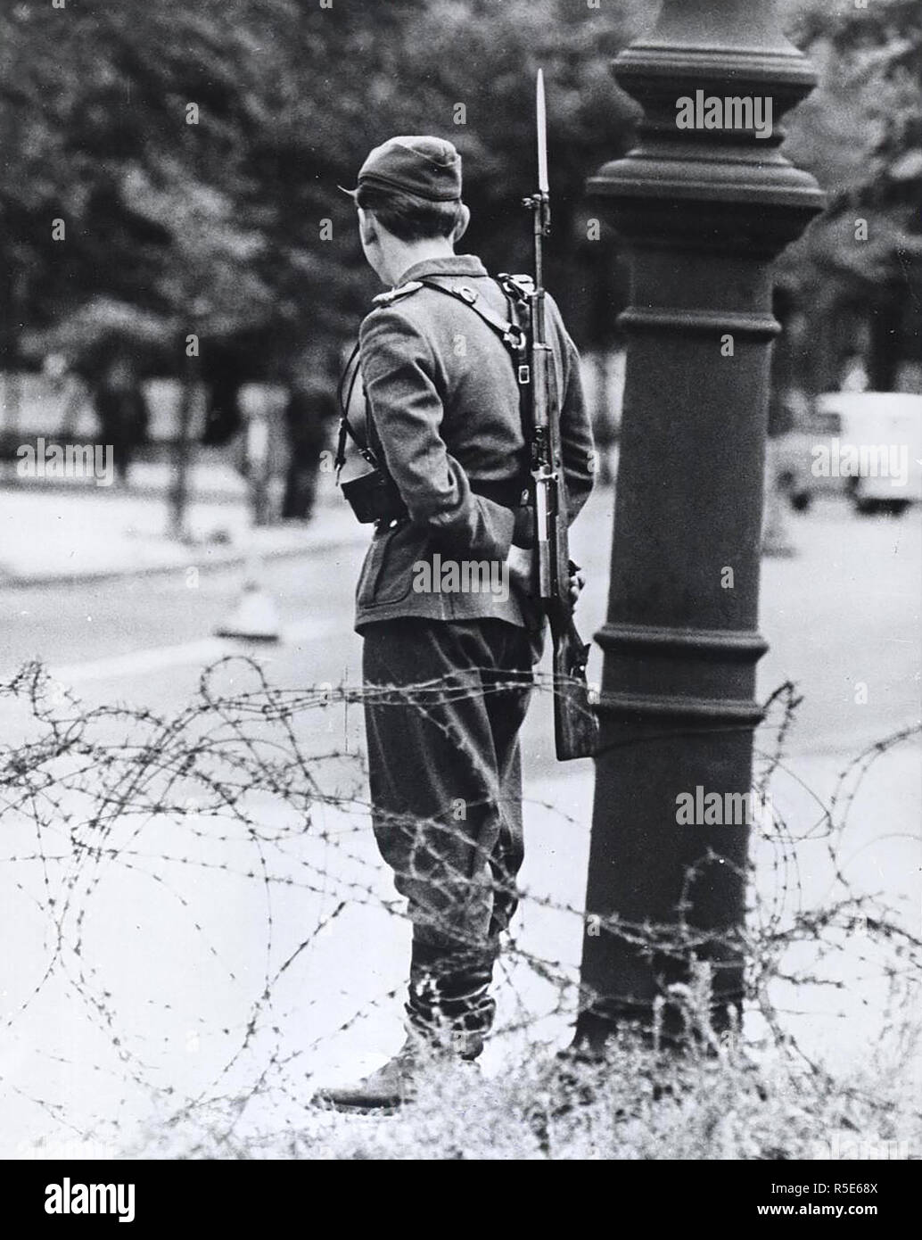 August 1961 - Wie eine triste Symbol der Unterdrückung, diese Teen-Aged Osten Deutscher Soldat Wache durch die geschlossene Grenze stehen Stockfoto