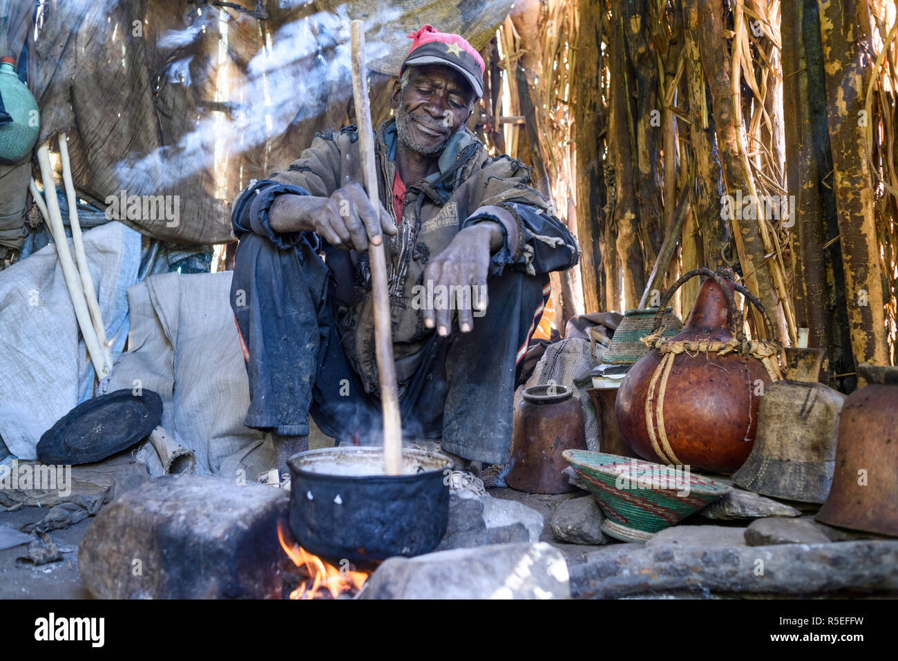 Muila Mann mittleren Alters Vorbereitung traditionelles Essen aus Hirse Mühle in einer einfachen Hütte voller Rauch. Stockfoto