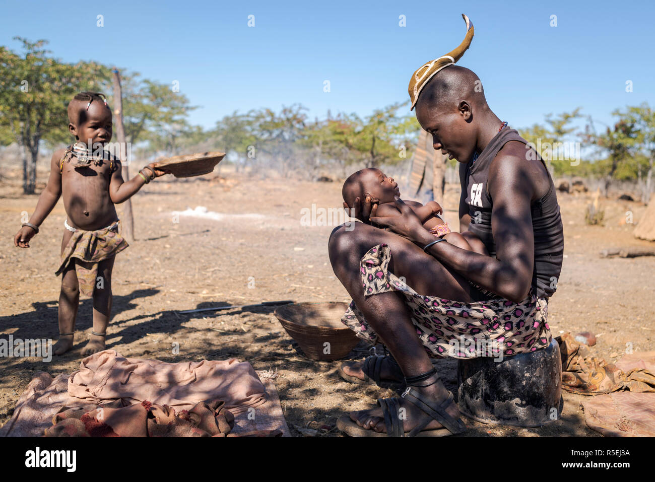 Junge Himba Junge Mit Einem Traditionellen Junge Himba Frisur Halt Ein Baby Auf Dem Schoss Wahrend Ein Kind Vorbei Wenn Man Sie Anschaut Stockfotografie Alamy