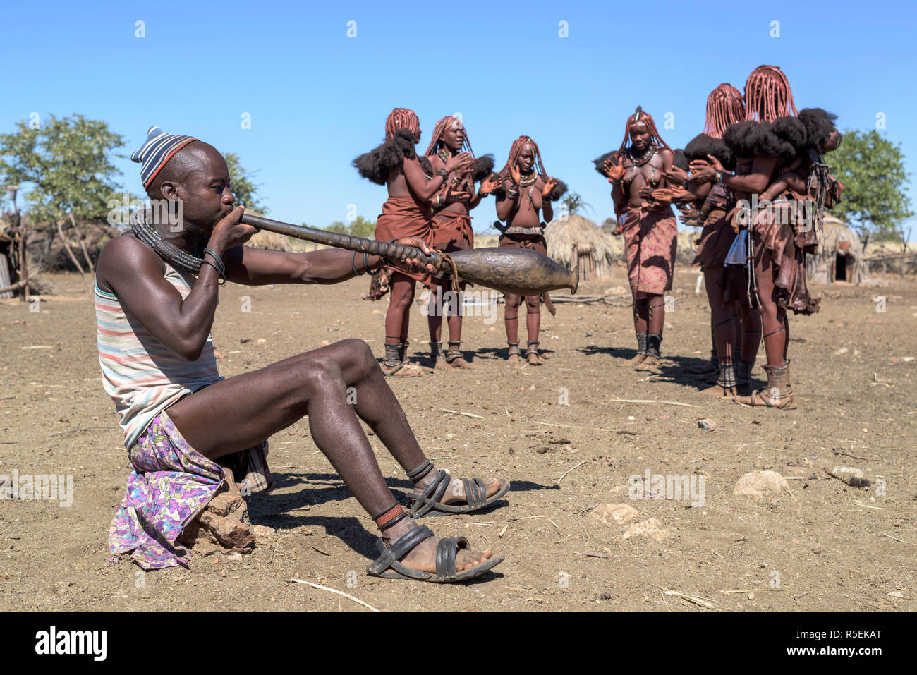 Gruppe von Frauen Himba mit traditionellen Kleider tanzen im Kreis, während ein Mann spielt eine Trompete aus einem orix Horn. Stockfoto