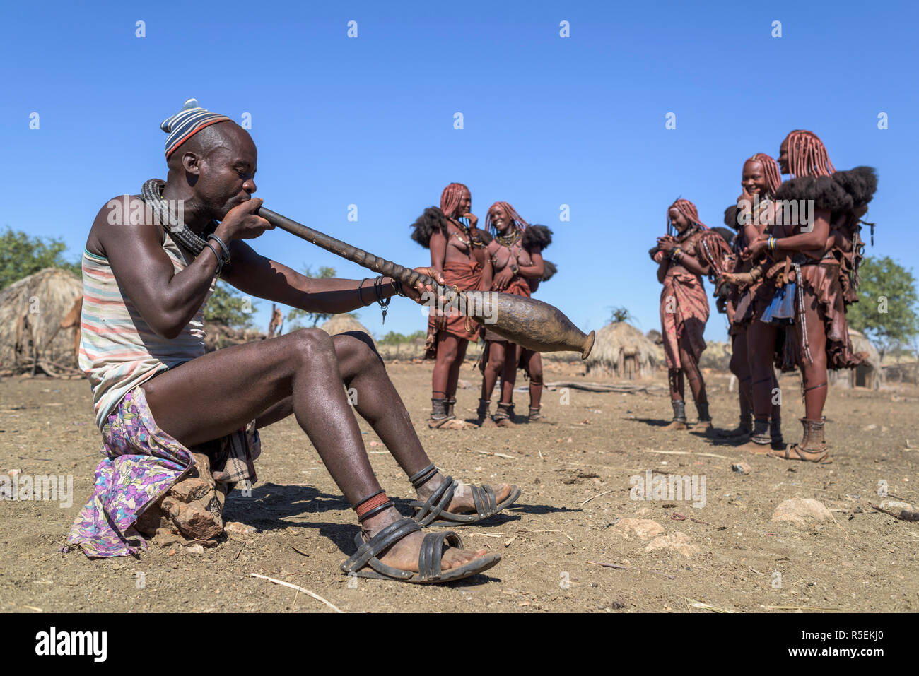 Gruppe von Frauen Himba mit traditionellen Kleider tanzen im Kreis, während ein Mann spielt eine Trompete aus einem orix Horn. Stockfoto