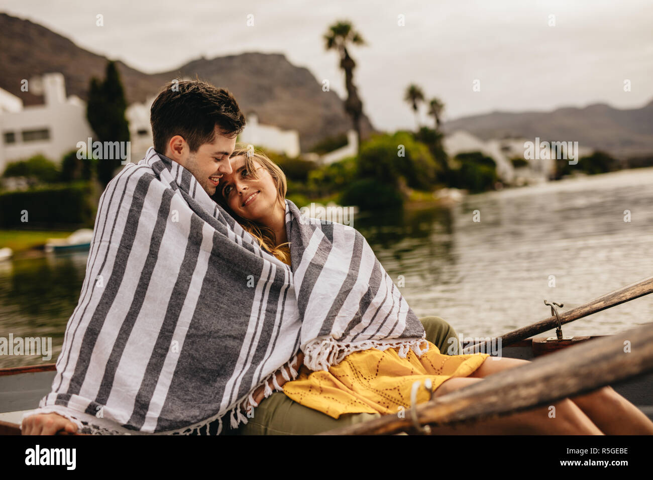 Junger Mann und Frau in Liebe in Boot zusammen in ein Handtuch gewickelt sitzen. Romantisches Paar auf einem Boot in einem See an einander mit der Liebe. Stockfoto