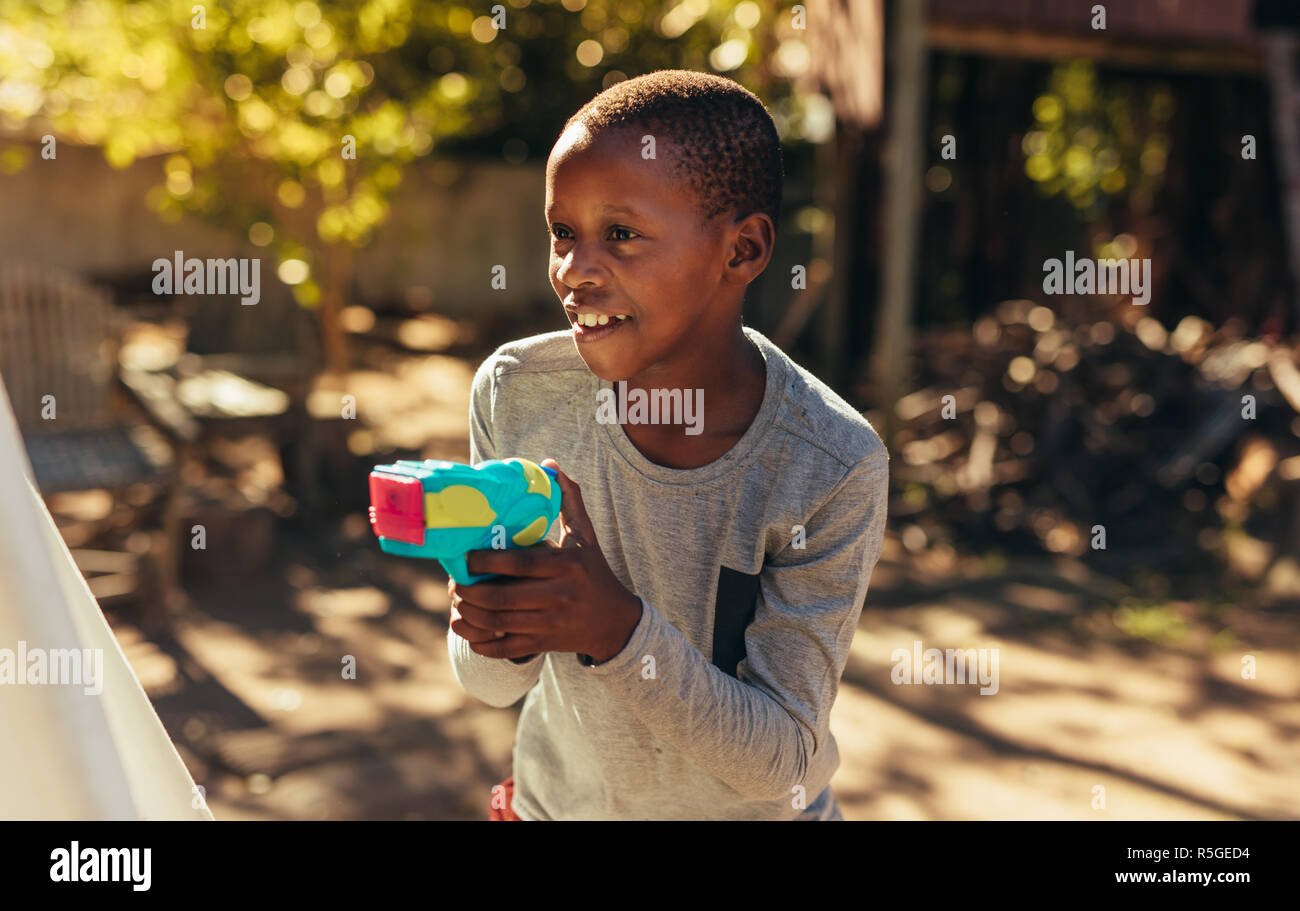 Kleinen afrikanischen Jungen spielen mit Wasser bespritzen Gun im Freien. Kid spielen mit Wasser Gewehr in den Hinterhof. Stockfoto