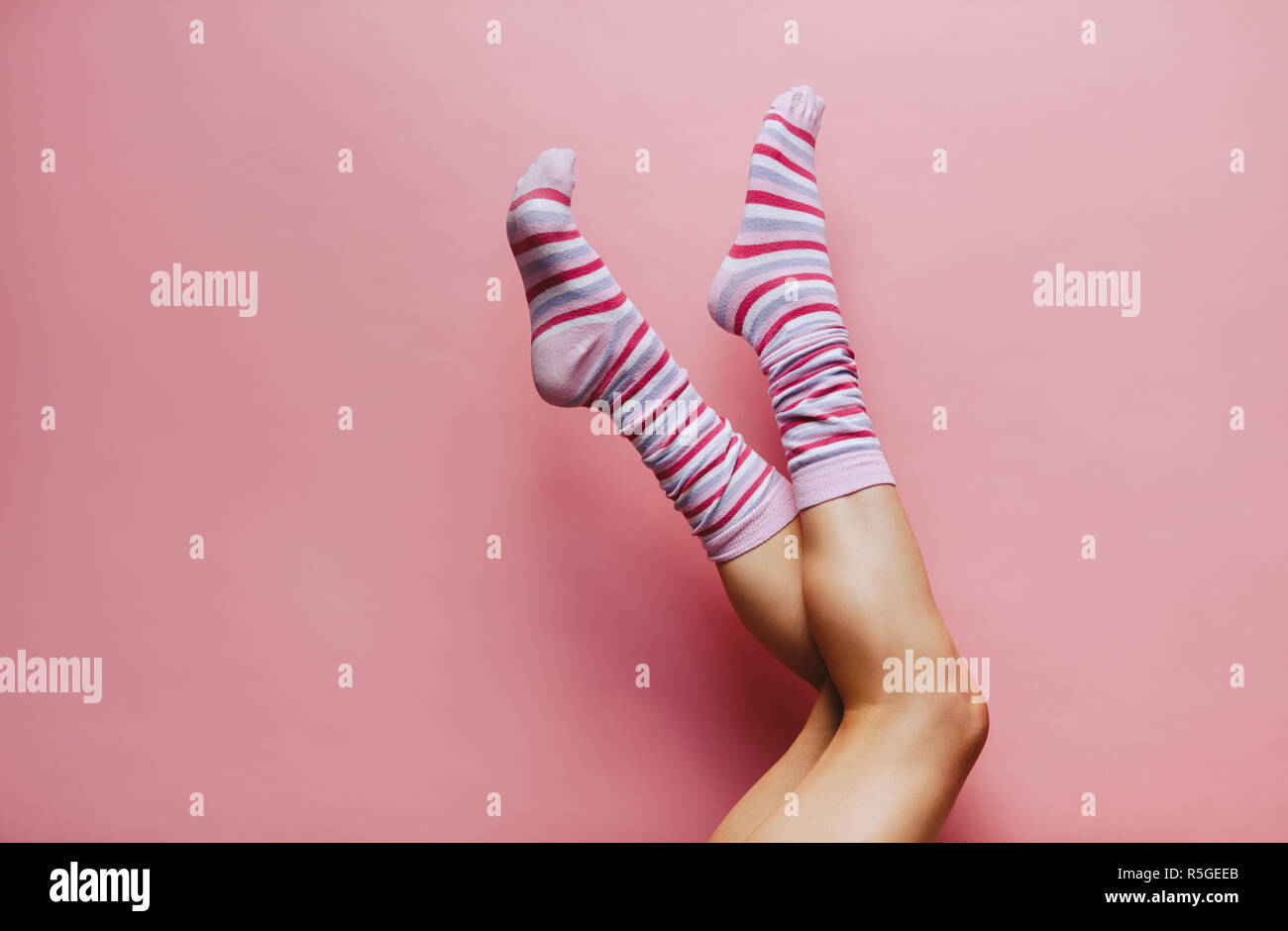 Weibliche Beine in bunten Socken auf rosa Hintergrund. Füße der Frau Socken tragen angehoben. Stockfoto