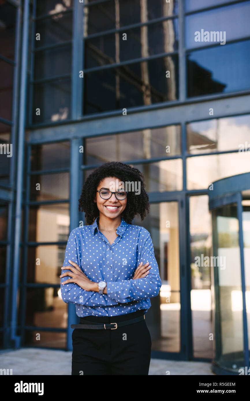 Portrait von selbstbewussten jungen Geschäftsfrau stehen außerhalb der Gebäude mit verschränkten Armen. Erfolgreiche weibliche Business Professional suchen Bei c Stockfoto