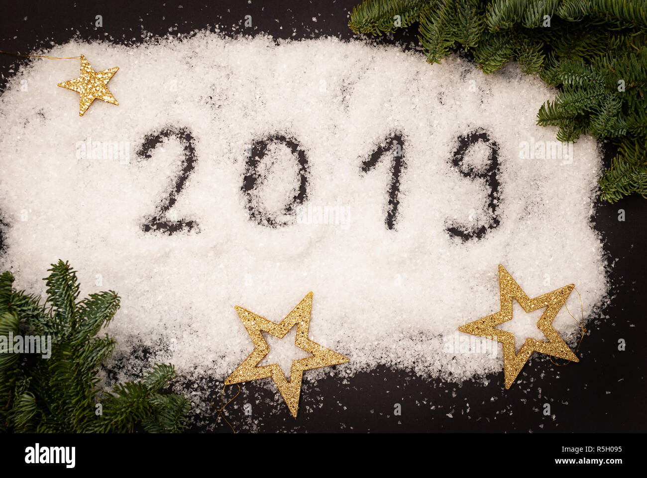 2019 im Schnee auf schwarzen Hintergrund mit grünen Zweigen und goldenen Sternen verziert geschrieben Stockfoto