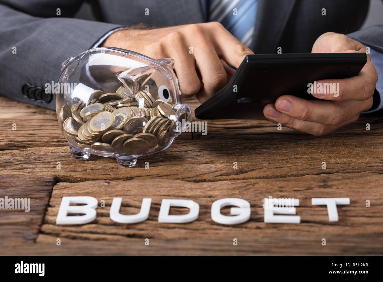 Geschäftsmann Berechnung des Budgets von sparschwein am Tisch Stockfoto
