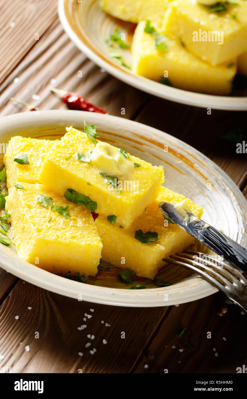 Polenta mit Butter und Grüns auf Ton Teller auf Holz- rustikalen Tisch Stockfoto