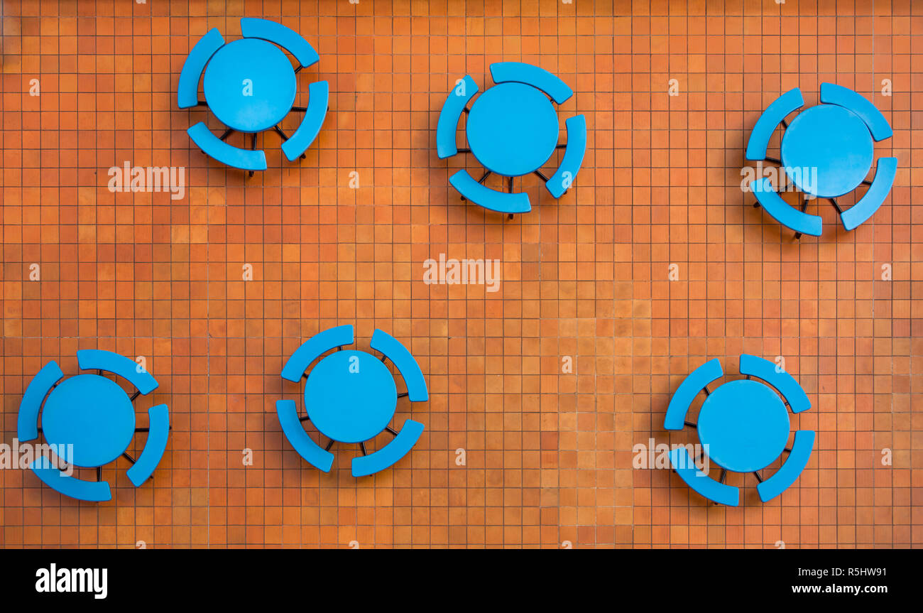 Orange Quadrat fliesen Terrasse und leer, runde blaue Tische in einen freien Food Court bieten markante Farbkontraste in einer zufälligen geometrischen Formen Muster. Stockfoto