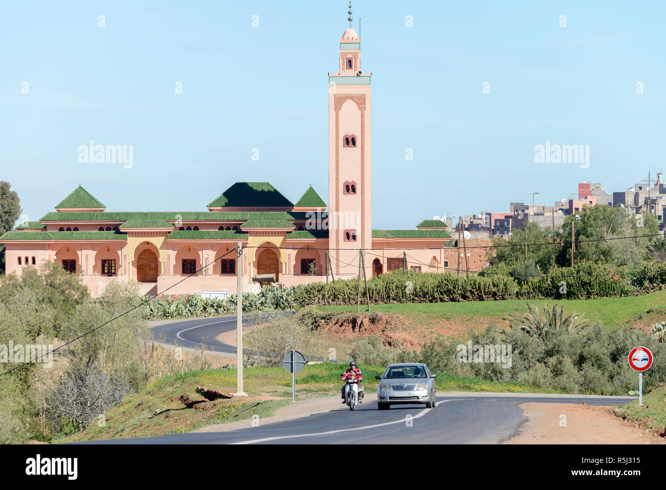 01-03-15, Marrakesch, Marokko. Eine Moschee und Minarett stehen als Kulisse zu einem entfernten Land Straße mit einem Auto und Roller entlang fahren in der sub-Atl Stockfoto