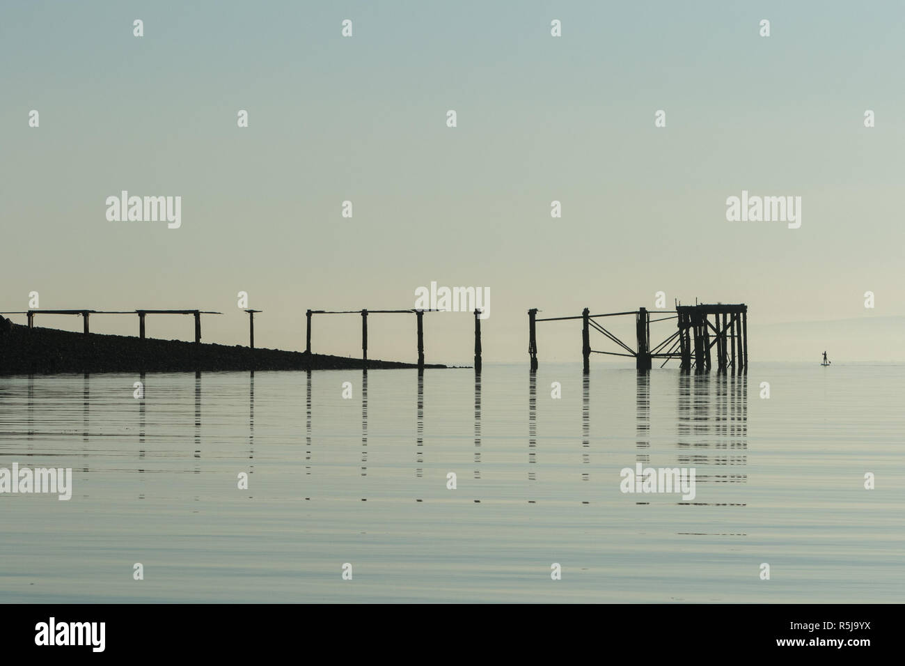 Silhouette einer Stand up Paddle boarder neben einem langen hölzernen Pier Stockfoto