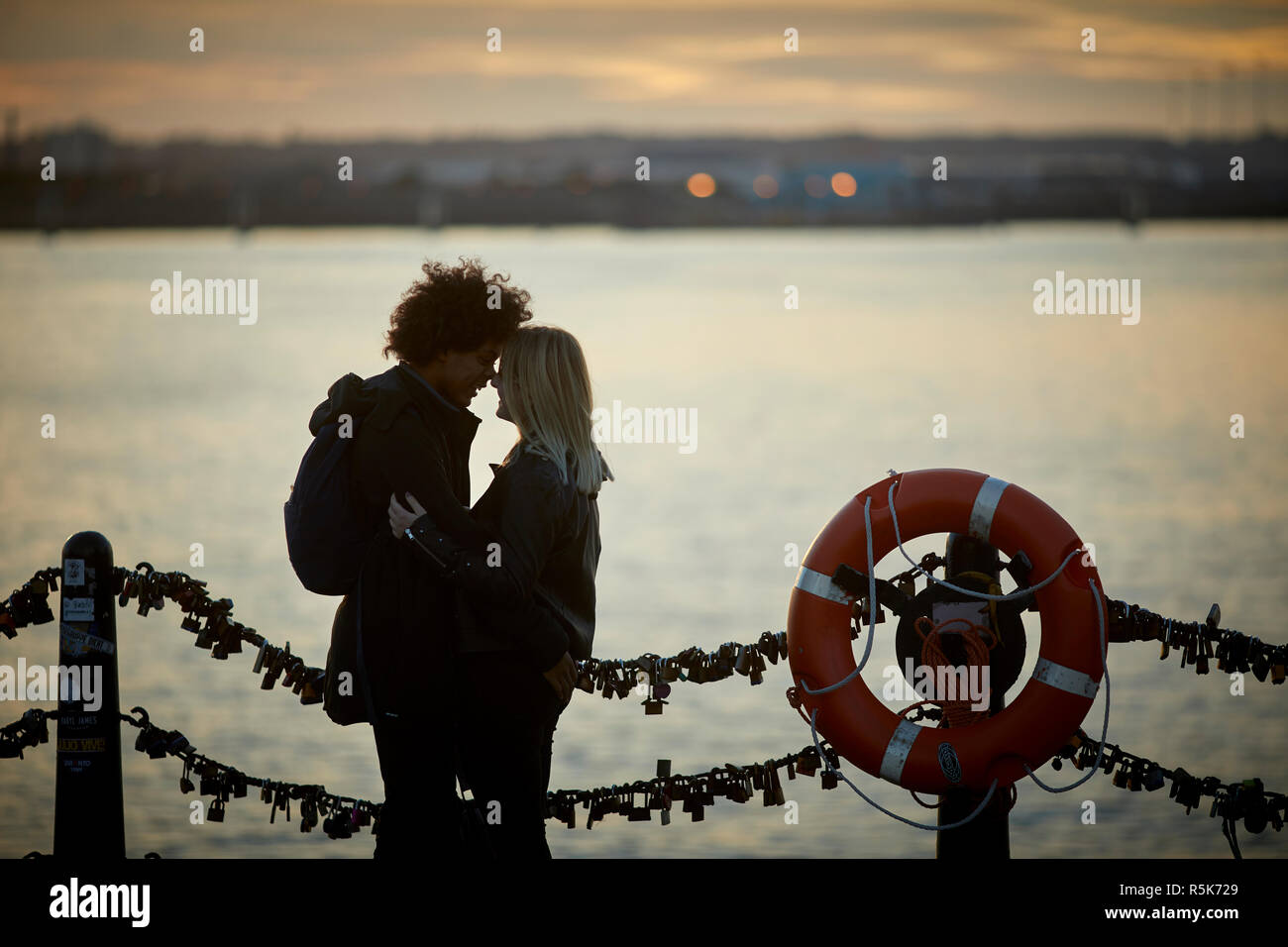 Pier Head Liverpool Waterfront mit Blick über den Fluss Mersey in Birkenhead bei Sonnenuntergang ein junges Paar kiss Stockfoto